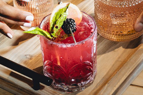 a red class with a blackberry and some leaves on the surface